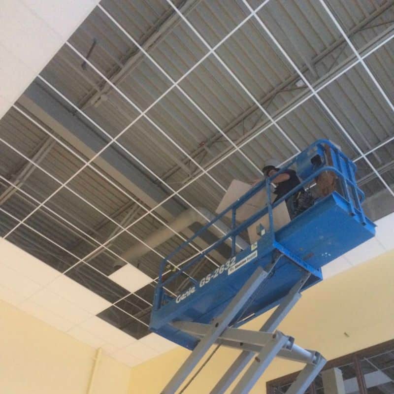 a drytech employee on a scissor lift installing a t-bar ceiling in a commercial building